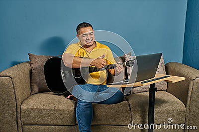 Hispanic man on a sofa in front of his laptop Greeting fellow students in the online guitar class Stock Photo