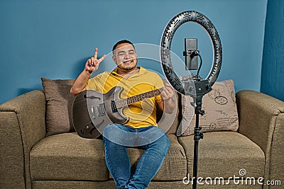 Hispanic man on a sofa in front of his tablet Greeting fellow students in the online guitar class Stock Photo