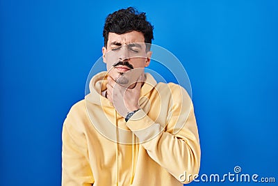 Hispanic man standing over blue background touching painful neck, sore throat for flu, clod and infection Stock Photo