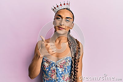 Hispanic man wearing make up and long hair wearing princess crown smiling happy and positive, thumb up doing excellent and Stock Photo