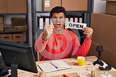 Hispanic man working at small business ecommerce holding open banner annoyed and frustrated shouting with anger, yelling crazy Stock Photo