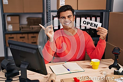 Hispanic man working at small business ecommerce holding open banner smiling happy pointing with hand and finger to the side Stock Photo