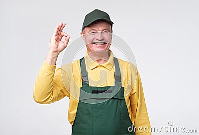 Hispanic mature mechanic in green cap and overalls standing smiling Stock Photo