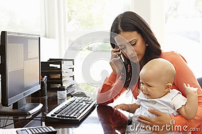 Hispanic mother with baby working in home office Stock Photo