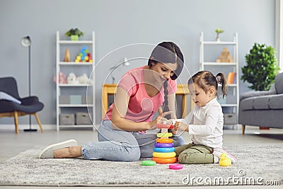 Hispanic mother and daughter play with toys while sitting on the floor in the room. Stock Photo