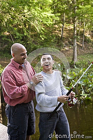 Hispanic teenager and father fishing in pond Stock Photo