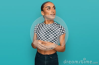 Hispanic transgender man wearing make up and long hair wearing modern clothes looking away to side with smile on face, natural Stock Photo