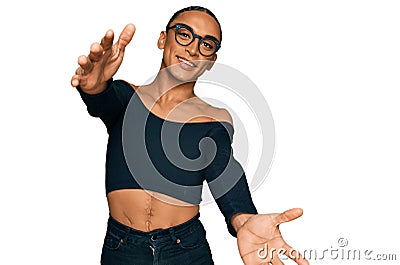 Hispanic transgender man wearing make up and long hair wearing women clothes looking at the camera smiling with open arms for hug Stock Photo
