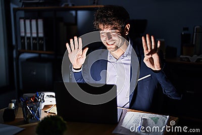 Hispanic young man working at the office at night showing and pointing up with fingers number nine while smiling confident and Stock Photo