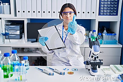 Hispanic young woman working at scientist laboratory showing middle finger, impolite and rude fuck off expression Stock Photo