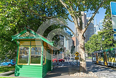 Historic green and yellow bus shelter building under London plane tree in city street view with passing tram and urban skyline Editorial Stock Photo