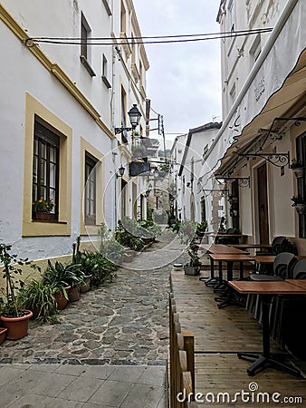 Historic, narrow spanish street with a restaurant terrace, guesthouse, flowers, and a street lamp Editorial Stock Photo