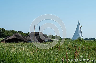 Historic thatched boathouses amongst the green reeds on Hickling Broad, east of Norwich, in Norfolk UK. Sailing boat on right. Stock Photo