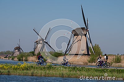 Historic windmills with cyclists cycling along the side of the canal in the foreground, at Kinderdijk, Holland Editorial Stock Photo