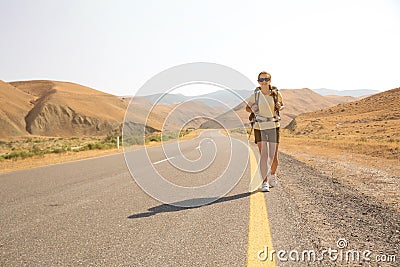 Hitchhiker traveler woman on the road in sunset. Girl traveler hiker on the road. Summer vacation. Freedom. Stock Photo