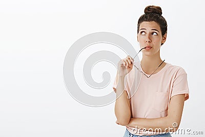 Hmm might work. Portrait of unsure hesitant cute tanned female with messy bun biting frame of eyewear gazing at upper Stock Photo