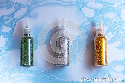 Set of emerald, silver and gold glitters in plastic bottles for soap making on the surface of blue marble, close up, full size, Stock Photo