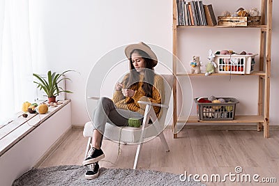 hobby and knit concept. pretty latin woman knitting at home. girl sitting on armchair looking autumn outside of window Stock Photo