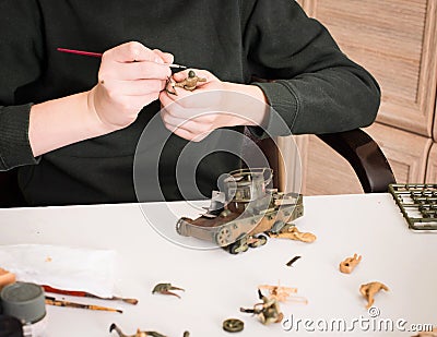 Hobby and leisure concept. Teen boy assembling and painting plastic models of soldiers and tank at workplace in his room. Stock Photo