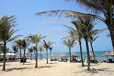 Hoi An, Da Nang, Vietnam - March 16, 2018: Tourists enjoying the sun on An Bang beach with lines of coconut trees, straw umbrellas Editorial Stock Photo