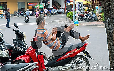 Hoi An, Vietnam - 28 Jul 2019: Man taking rest on motorbike. Scooter driver with smartphone in hands Editorial Stock Photo