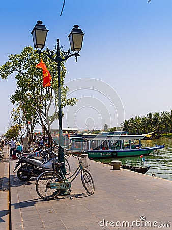 HOIAN, VIETNAM, SEPTEMBER, 04 2017: Bikes and motorcycles parked in a row, and some boats ofr tourist in the water in Editorial Stock Photo