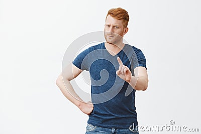 Hold on, I forbid you. Strict serious-looking young dad with ginger hair and beard waving index finger and staring Stock Photo