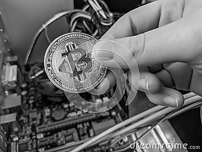 Holding a bitcoin in black and white among computer hardware, electronics and wires representing cryptocurrencies, mining and Stock Photo