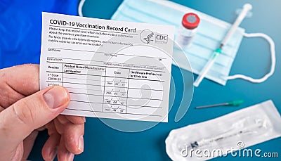 Holding a Covid-10 vaccination record card with vaccine vial, syringe and facial mask and faqs Stock Photo