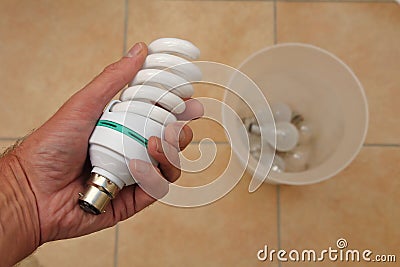 Holding a low energy CFL light bulb with discarded tungsten bulbs in background Stock Photo