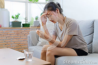 Young Asian women on sofa closing her eyes are suffering from headache and have some fever. Stock Photo