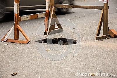 Hole in asphalt on automotive roadway street. Pit in road surface, is surrounded by building fence construction with warning tape Stock Photo