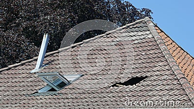 Hole in the roof of a house. Roof damage. Broken tile roof after a storm. Stock Photo