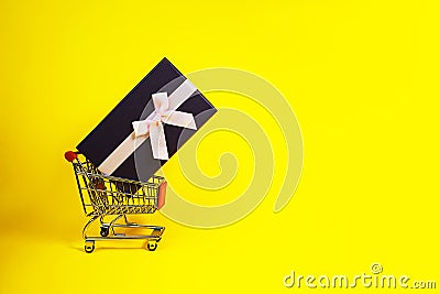 Holiday gift, Black Friday concept with gift box and pink bow in a metal shopping trolley, basket on yellow color Stock Photo