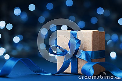 Holiday gift box or present with bow ribbon against blue bokeh background. Magic christmas greeting card. Stock Photo