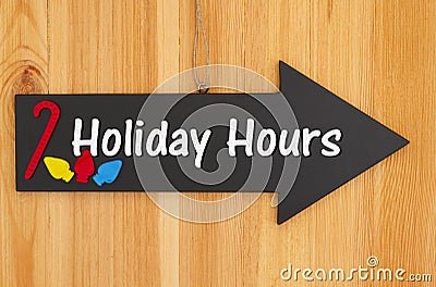 Holiday Hours type message on hanging arrow chalkboard sign with a candy cane and lights Stock Photo