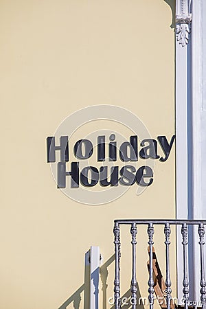 Holiday house. Hotel words text posted on the exterior wall. Near the railing of a balcony. Yellow wall Stock Photo