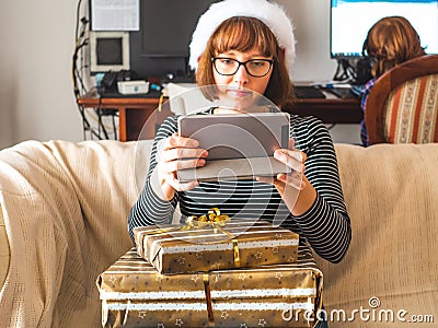 Young woman with stacked gifts looking at tablet on couch Stock Photo