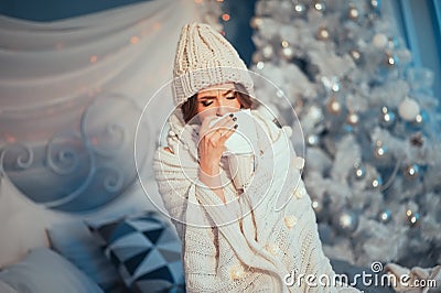 Holiday is ruined! Young beautiful woman in knitted hat and scarf rolled in plaid having flu and blowing her nose at handkerchief Stock Photo
