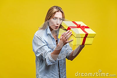 Holiday surprise. Portrait of astonished curious woman in denim shirt looking inside gift box. studio shot on yellow Stock Photo