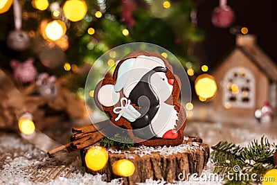 Holiday traditional food bakery. Gingerbread little pinguin in christmas hat with gift in cozy warm decoration with garland lights Stock Photo