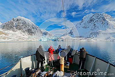 Holiday travel in Arctic, Svalbard, Norway. People on the boat. Winter mountain with snow, blue glacier ice with sea in the foregr Editorial Stock Photo