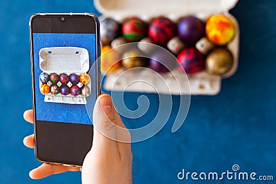 Holidays, tradition, technology and people concept - close up of man hands with smartphone taking picture of colored easter eggs Stock Photo