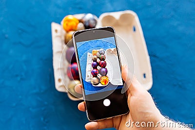 Holidays, tradition, technology and people concept - close up of man hands with smartphone taking picture of colored easter eggs Stock Photo