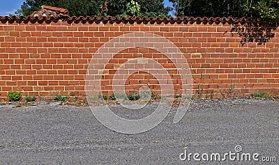 Hollow brick wall with terracotta roof tiles on top. Asphalt road in front. Stock Photo