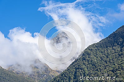 Hollyford River Valley between mountains and peaks with low cloud against blue sky Stock Photo