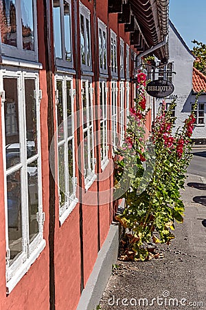 Hollyhocks and roses growing in front of the traditional red cottage house in Svaneke. Editorial Stock Photo