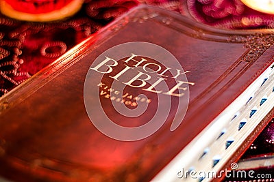 Holy Bible with pressed decorative leather cover on table with soft flickering candlelight Stock Photo