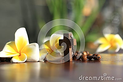 Holy Cross of rosary closeup in low angle view. Wooden rosary with Jesus Christ crucifix and Bali frangipani flowers. Copy space. Stock Photo