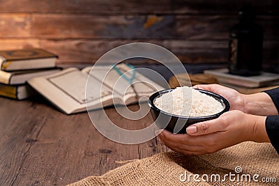 Holy Quran and a grain of rice in a wooden bowl in the sack on a wooden table, Islamic zakat concept. Stock Photo